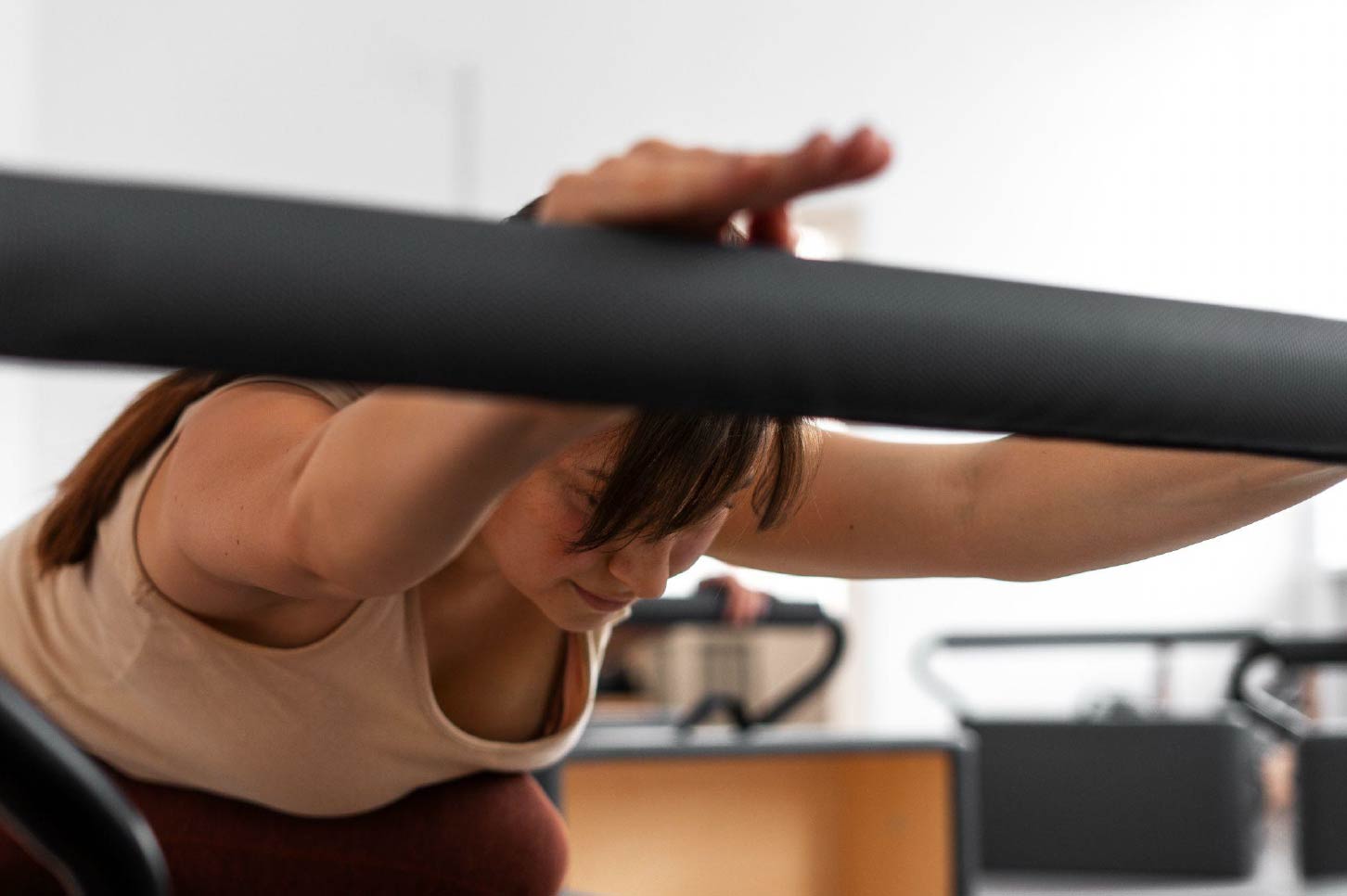 Mujer realizando un estiramiento con brazos extendidos sobre una barra durante una clase de pilates en estudio interior para mejorar el sistema linfático